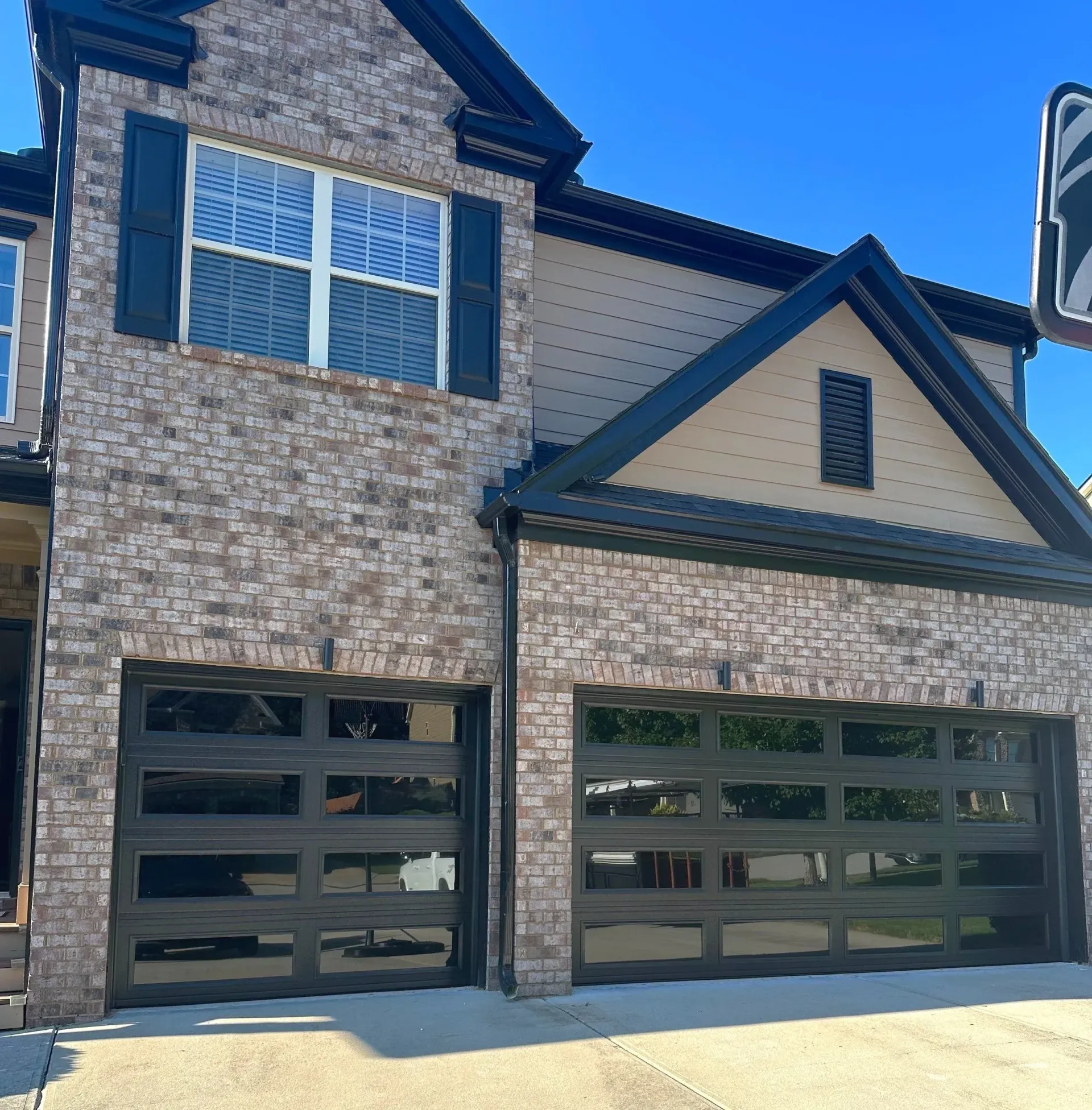 Two-story brick townhome with black garage doors and shutters, under a clear blue sky.