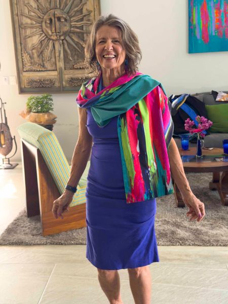 Woman in a blue dress and colorful scarf smiling in a bright living room