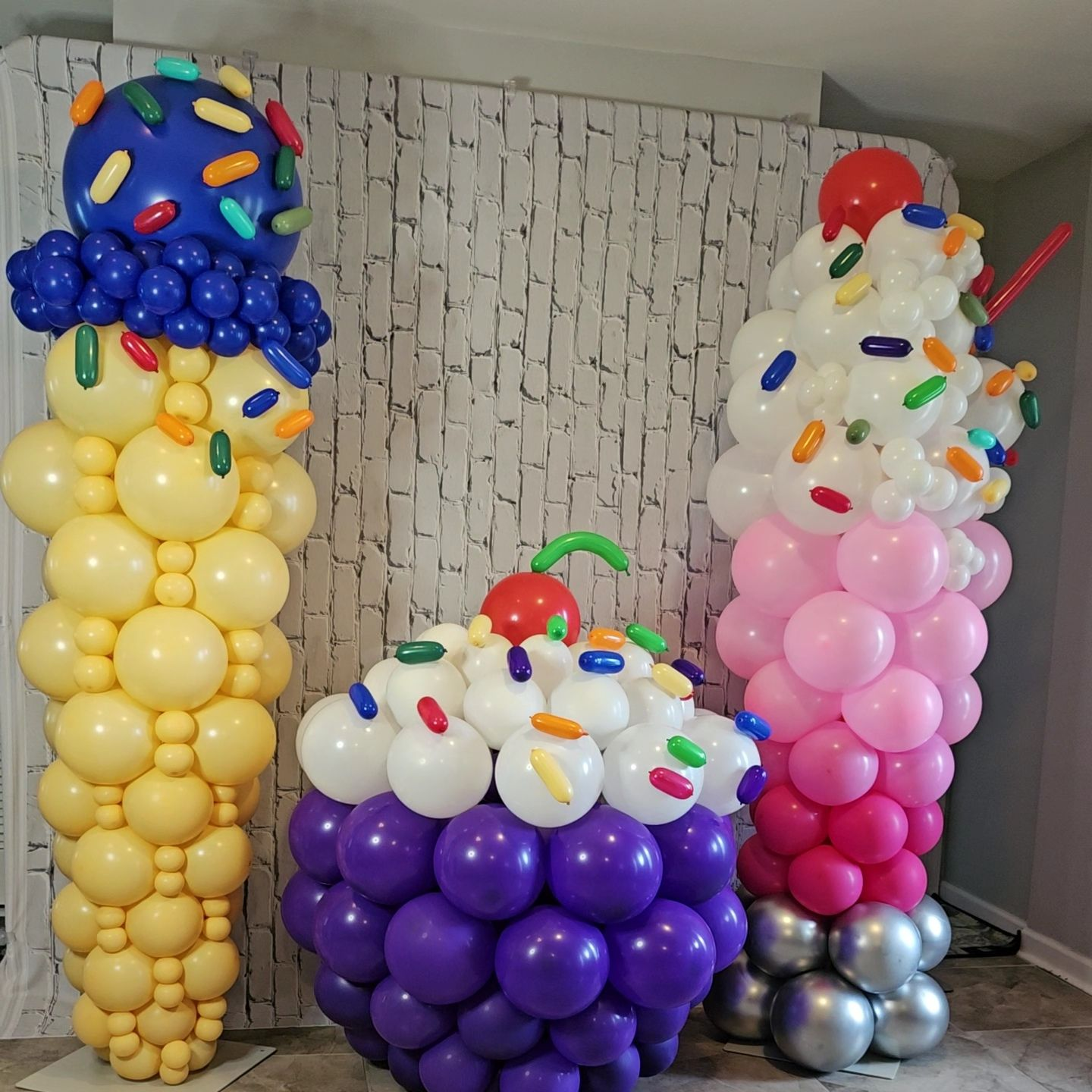Balloon sculptures of an ice cream cone, cupcake, and sundae created by My Life In Balloons LLC. Features bright yellow, purple, pink, and white balloons with colorful sprinkles and metallic accents. Perfect for dessert-themed parties, birthdays, or candy shop events.