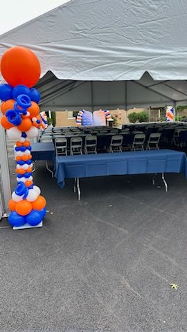 Orange, blue, and white balloon arch created by My Life In Balloons LLC for GGB’s 125th anniversary event. Arch frames a branded step-and-repeat backdrop for a photo area.