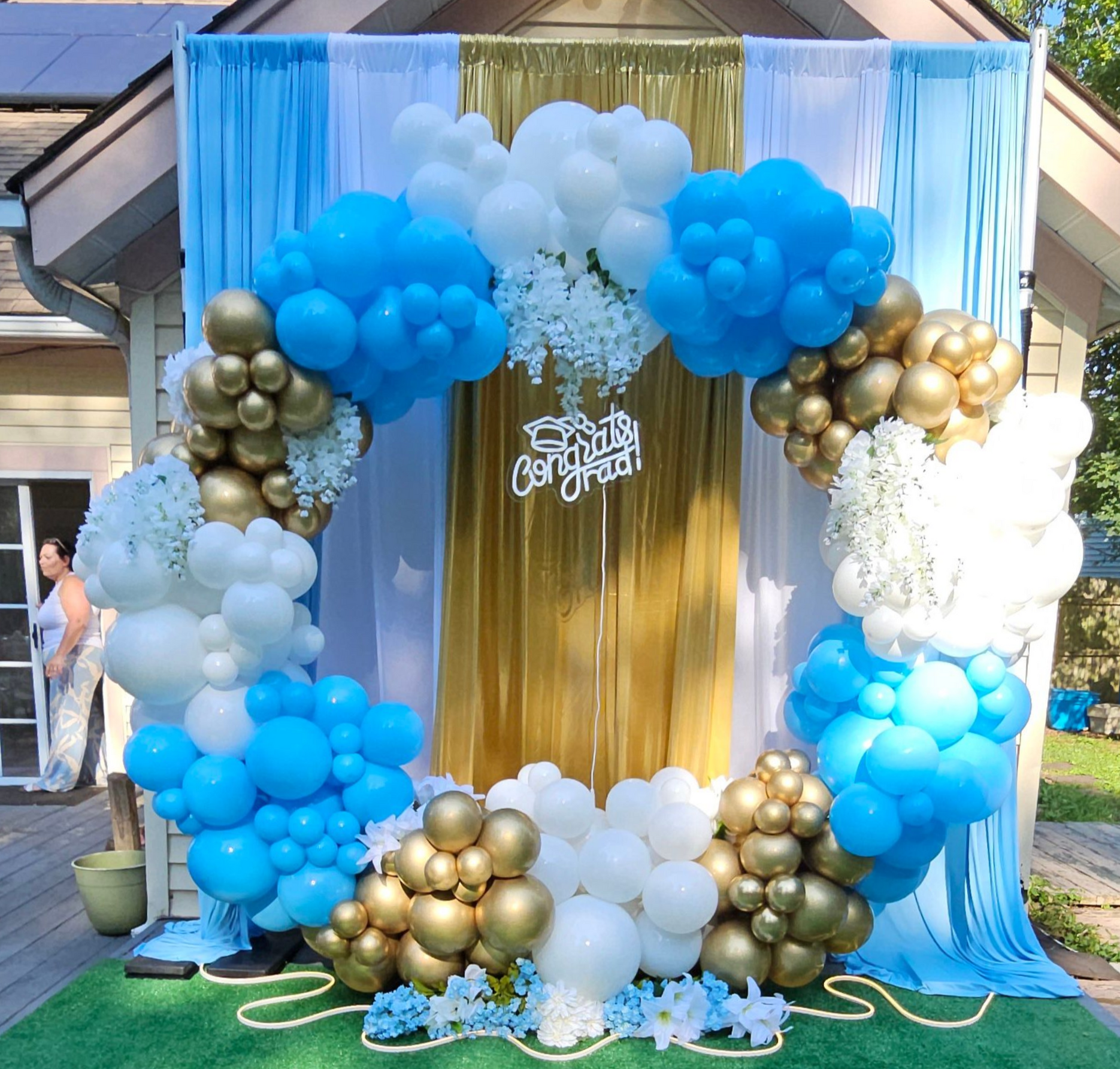 Graduation balloon tower with curly spirals and custom topper “Congrats Addiana” in blue, white, and gold by My Life In Balloons LLC.