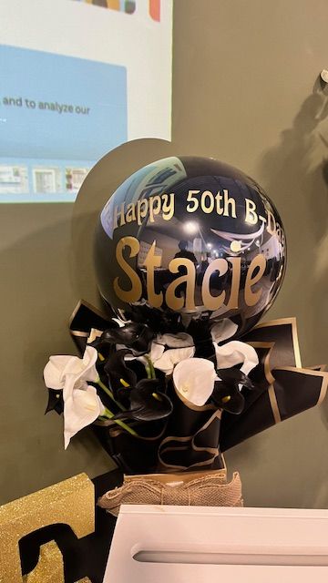 Custom black and gold balloon bouquet created by My Life In Balloons LLC for a 50th birthday celebration. Features personalized text and floral accents.