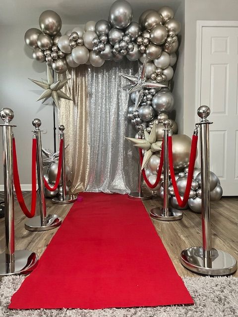 Prom sendoff balloon arch and backdrop setup by My Life In Balloons LLC, featuring silver and chrome balloons, metallic stars, and a red carpet entrance for a glamorous photo moment.