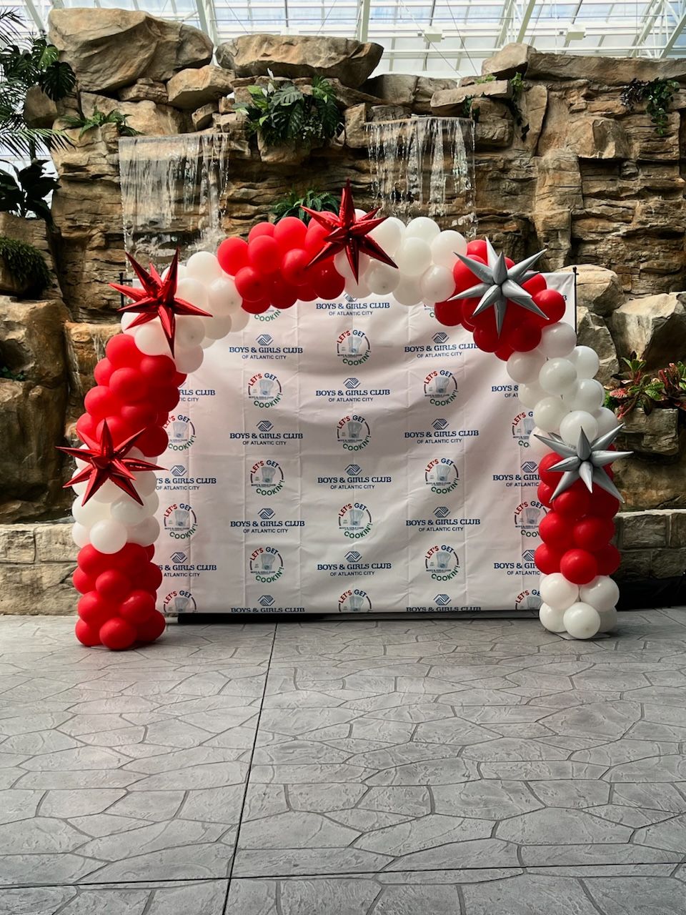 Red and white balloon arch with metallic starbursts by My Life In Balloons LLC for Let’s Get Cookin’ 2024 at Showboat, Atlantic City.