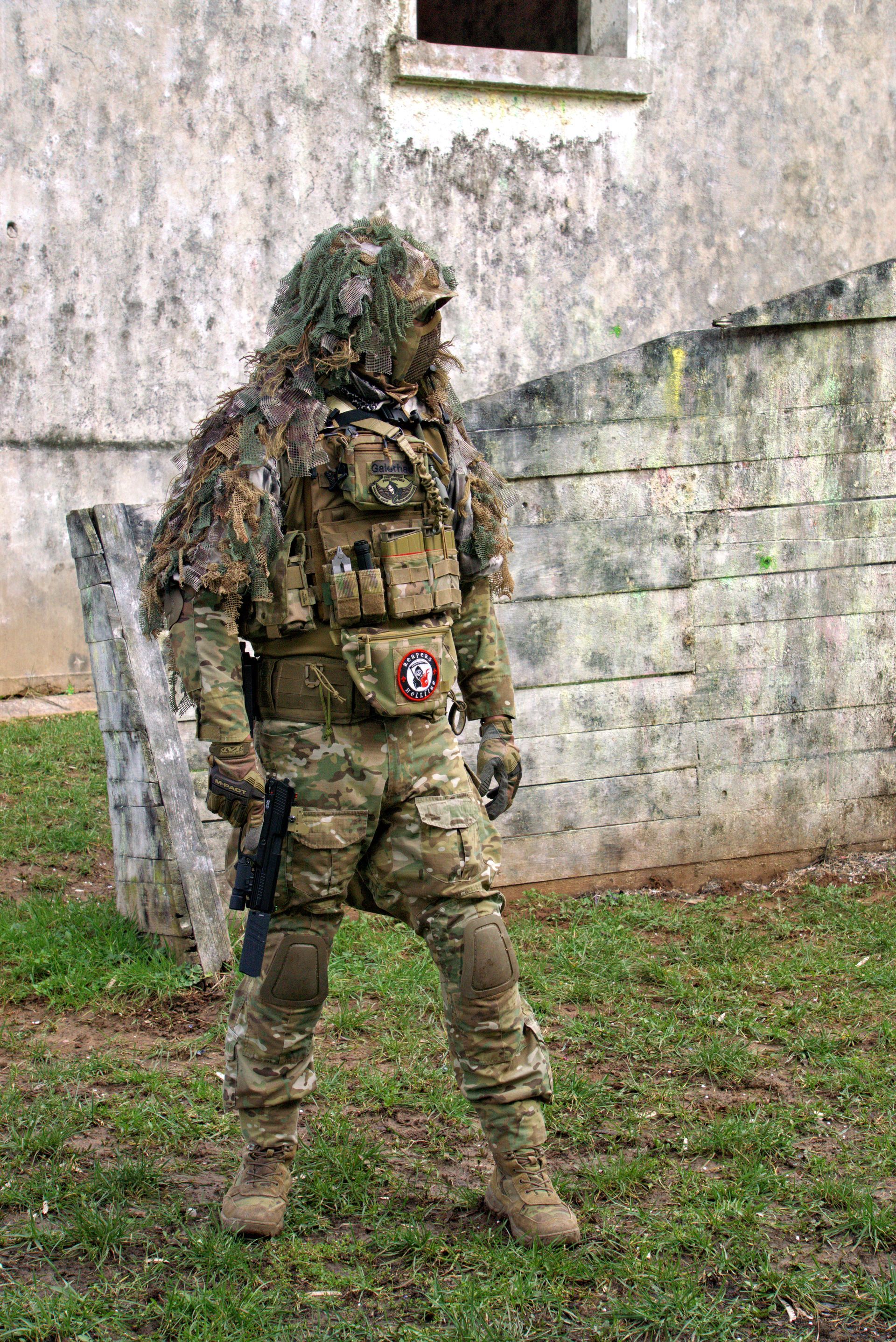 Ein Soldat im Tarnanzug steht im Gras vor einem Gebäude.