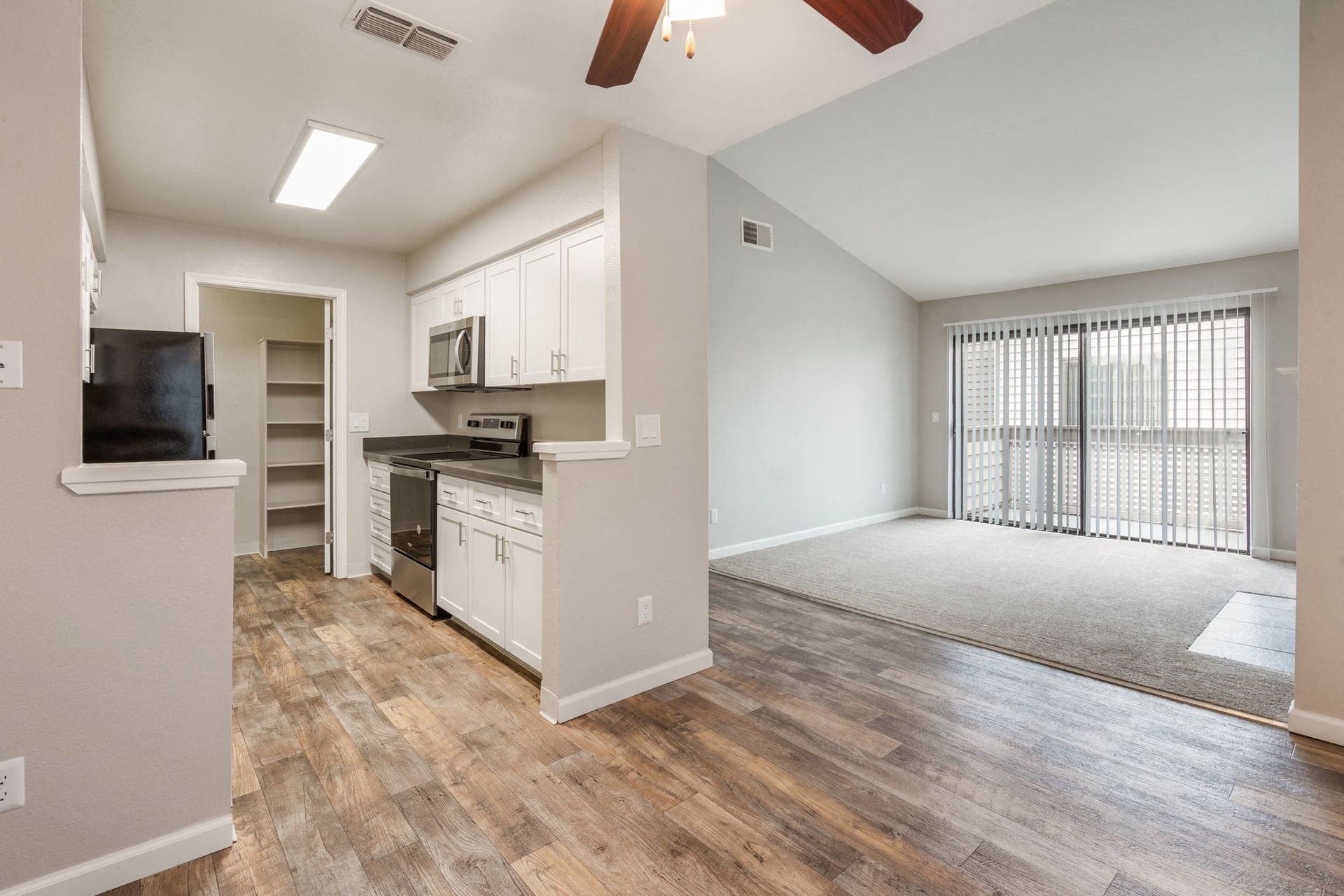 Open-concept kitchen and living area with white cabinets, stainless-steel appliances, and a sliding balcony door at Hidden Lake apartments in Sacramento, CA.