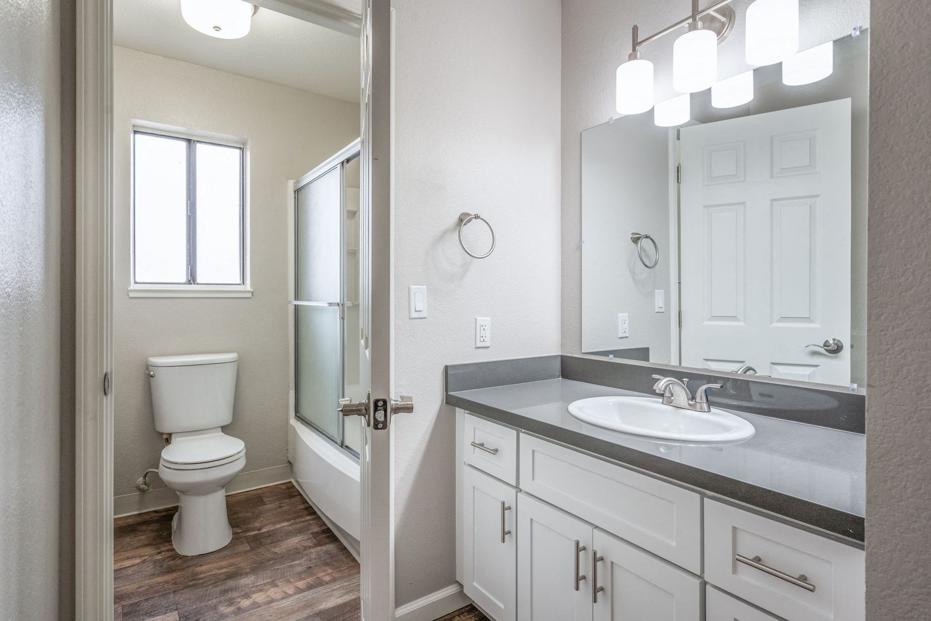 Bathroom interior with a white vanity, gray countertop, mirror, toilet, and glass-enclosed shower at Hidden Lake apartments in Sacramento, CA.