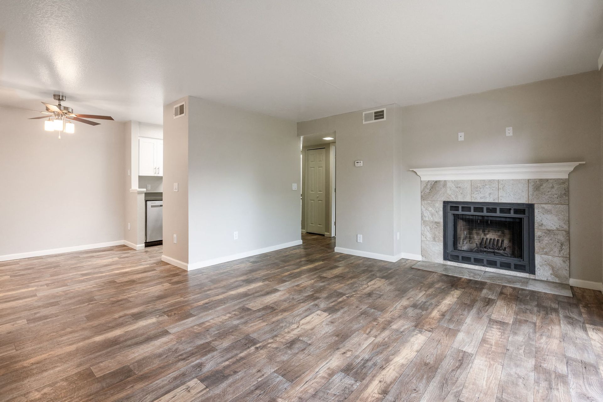 Living room with wood-look flooring, neutral walls, a ceiling fan, and a fireplace on the right at Hidden Lake apartments in Sacramento, CA.