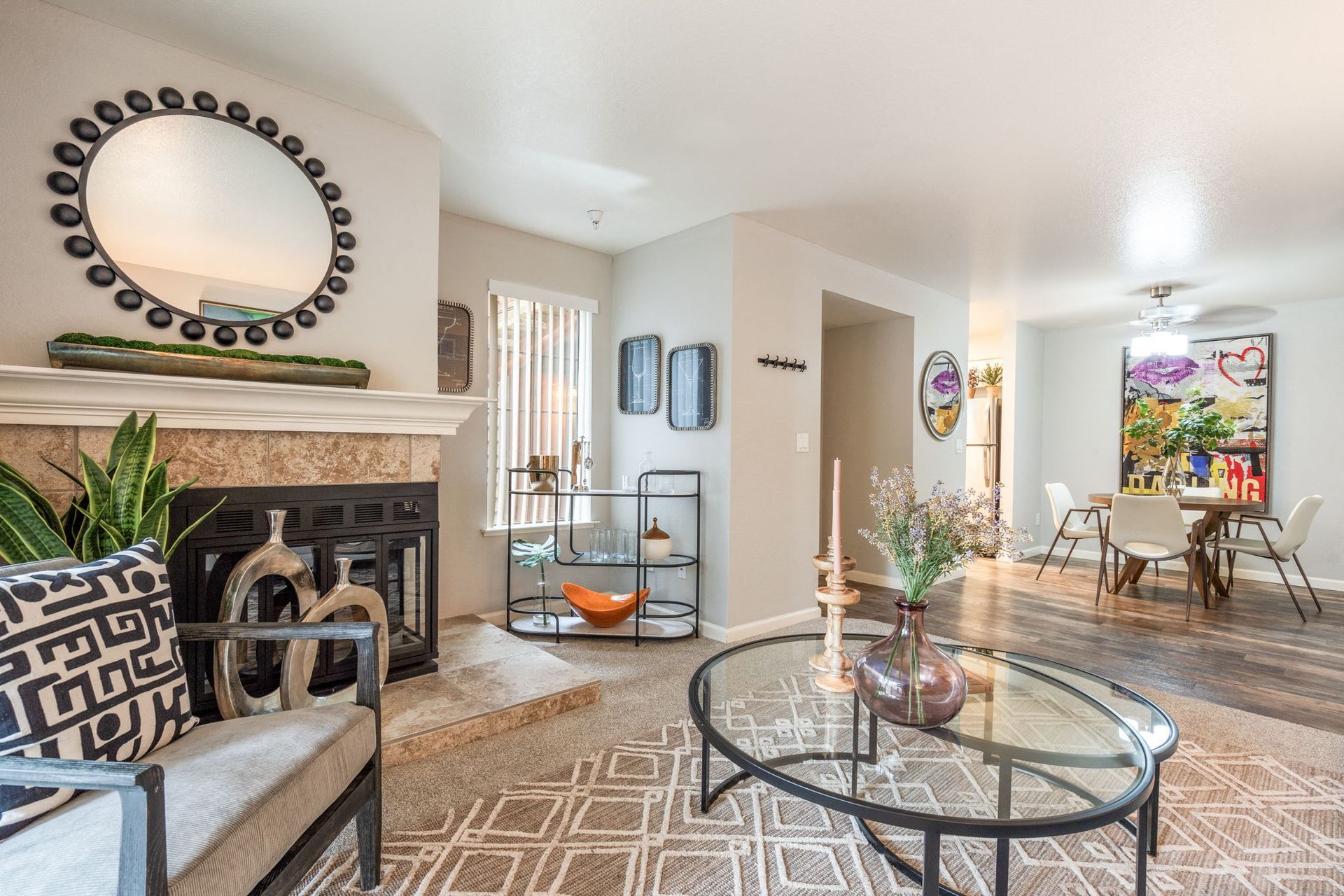 Living room with fireplace, round mirror, plants, and a dining area in a modern apartment at Hidden Lake apartments in Sacramento, CA.
