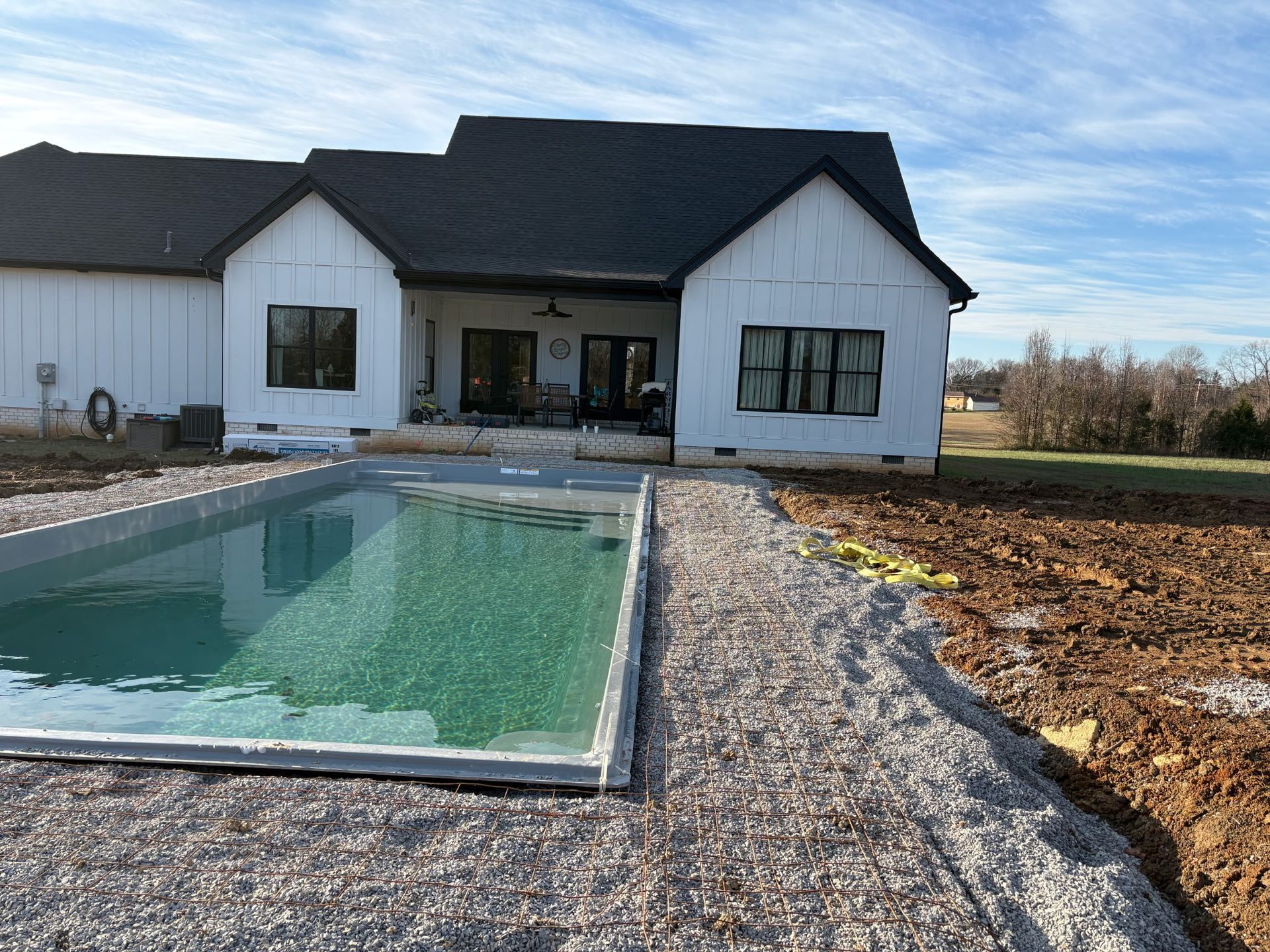 Modern white house with black roof beside a rectangular swimming pool and gravel landscaping