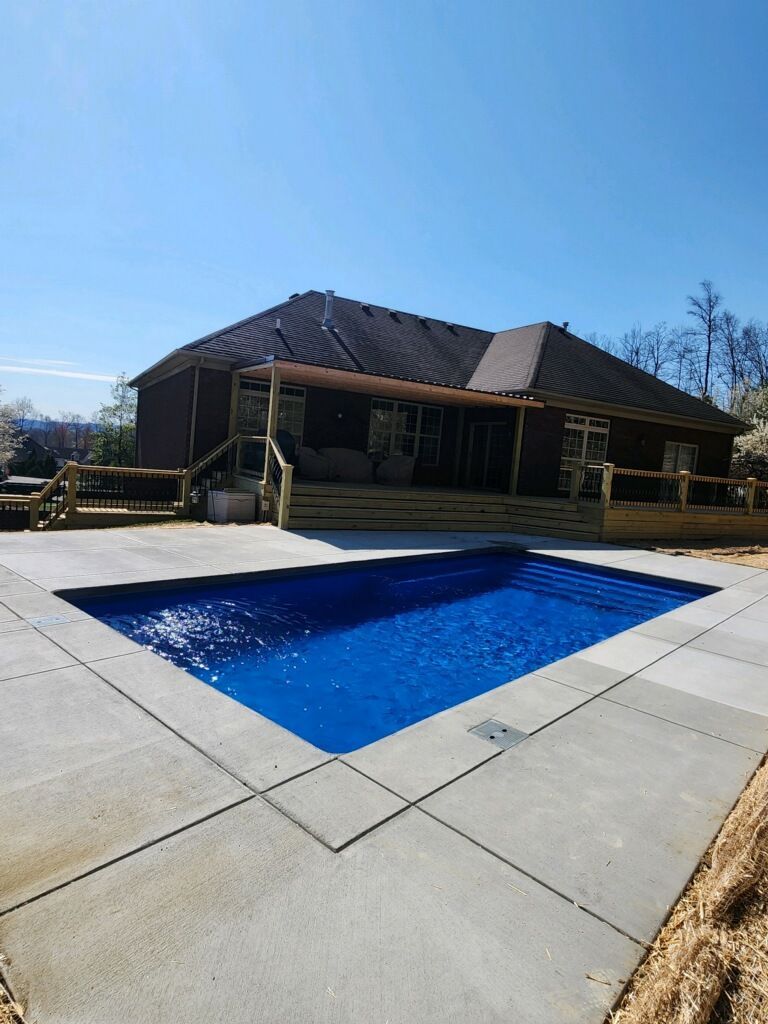 Backyard patio with a rectangular in-ground pool beside a brick house under a clear blue sky