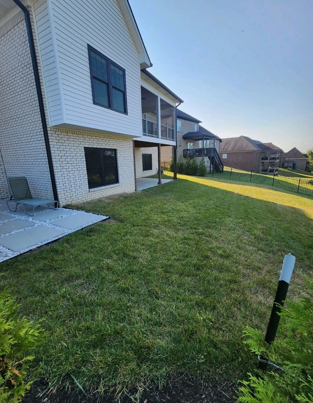 Backyard of a white apartment building with green lawn, patio, and distant hills under a blue sky
