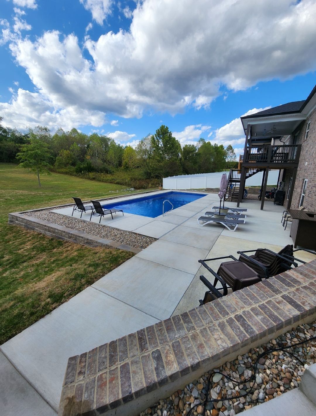 Poolside patio with pool. Blue pool, concrete patio, brick border, lawn, blue sky.