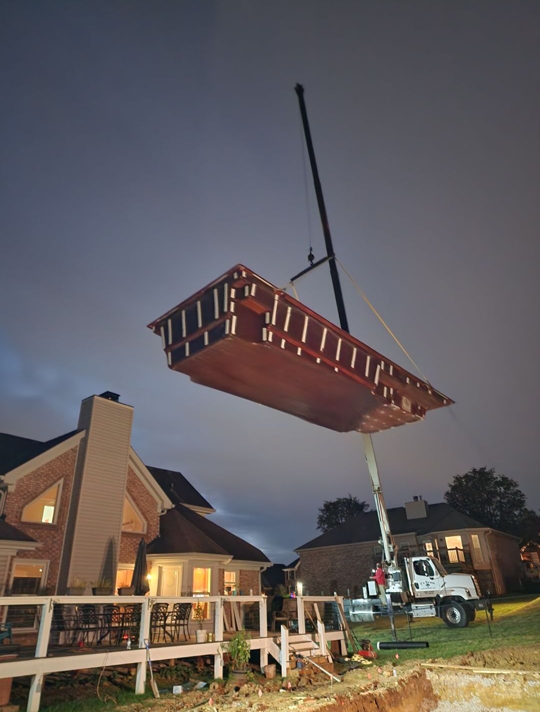A crane lifts a wooden structure above a house at night.