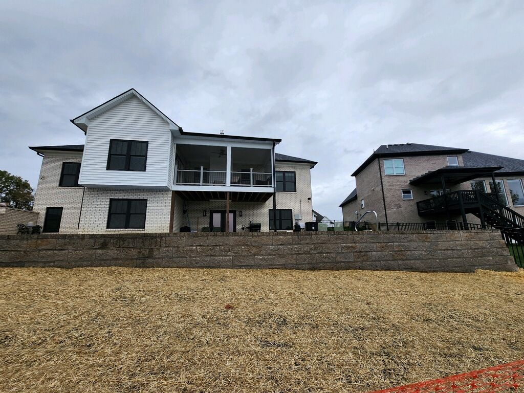 Two-story house with stone retaining wall and gravel yard under cloudy sky