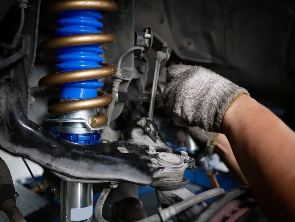 A Person Is Working on A Shock Absorber on A Car — Tweed Exhaust & Mechanical In Tweed Heads South, NSW