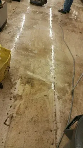 Dirty floor being cleaned with a machine. Muddy water and debris on the floor with a person in the background.