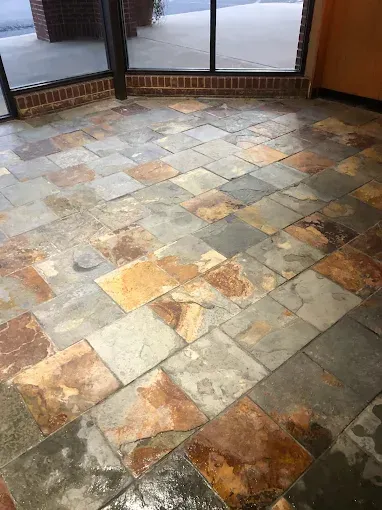 Slate tile floor in a commercial space, featuring varying colors and a wet appearance near the entrance.