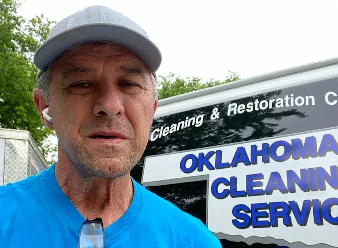 Man in a blue shirt and cap, in front of a van with 