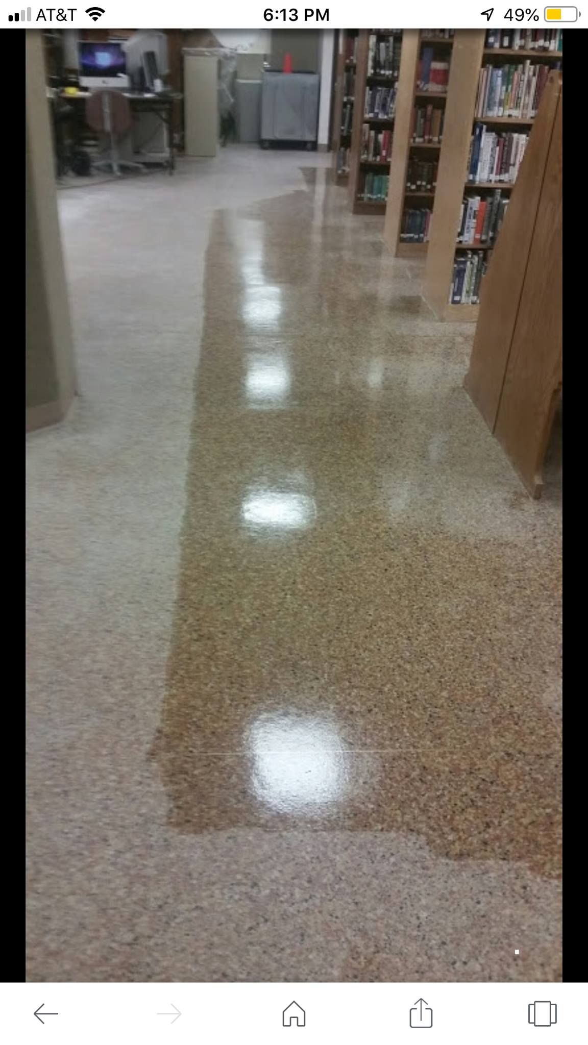 Wet, polished floor in a library aisle reflects overhead lights. Light-colored stone floor. Book shelves are visible.