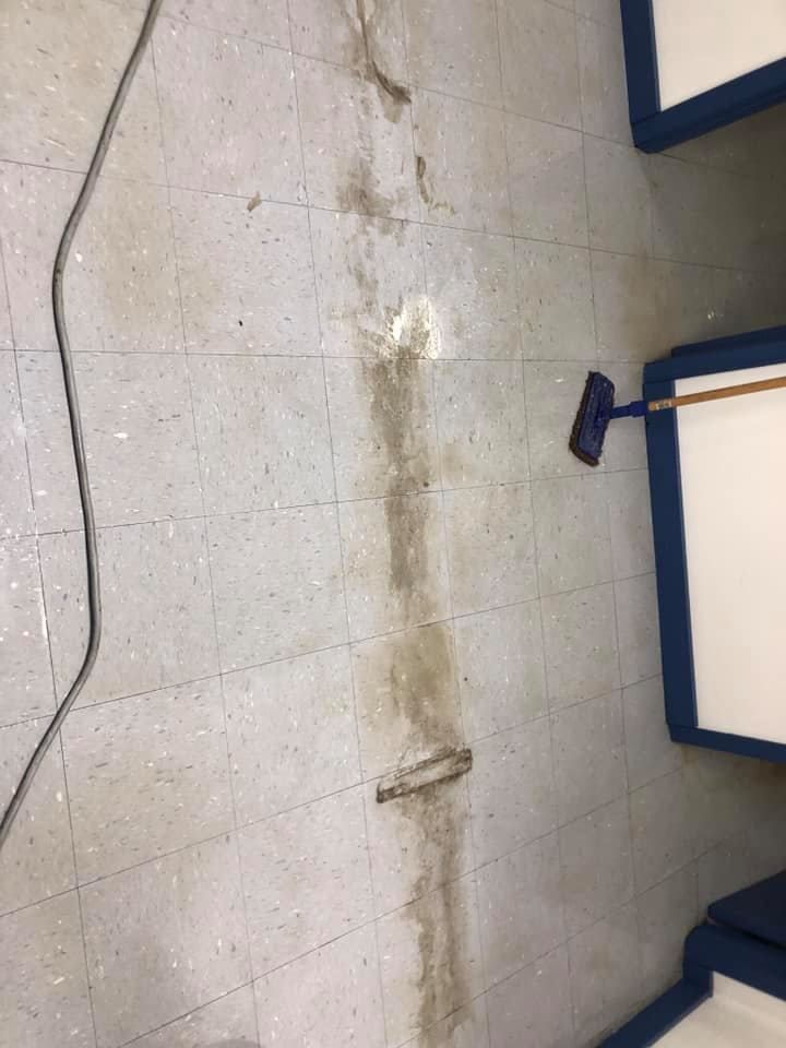 Floor with dark stain, potentially water damage, near a wall with blue trim and a power cord.