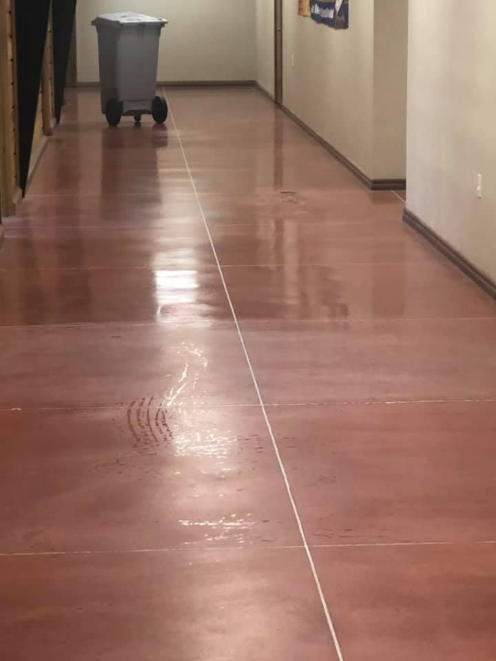 Long hallway with reddish-brown polished concrete floor, white line down the center, gray trash bin.