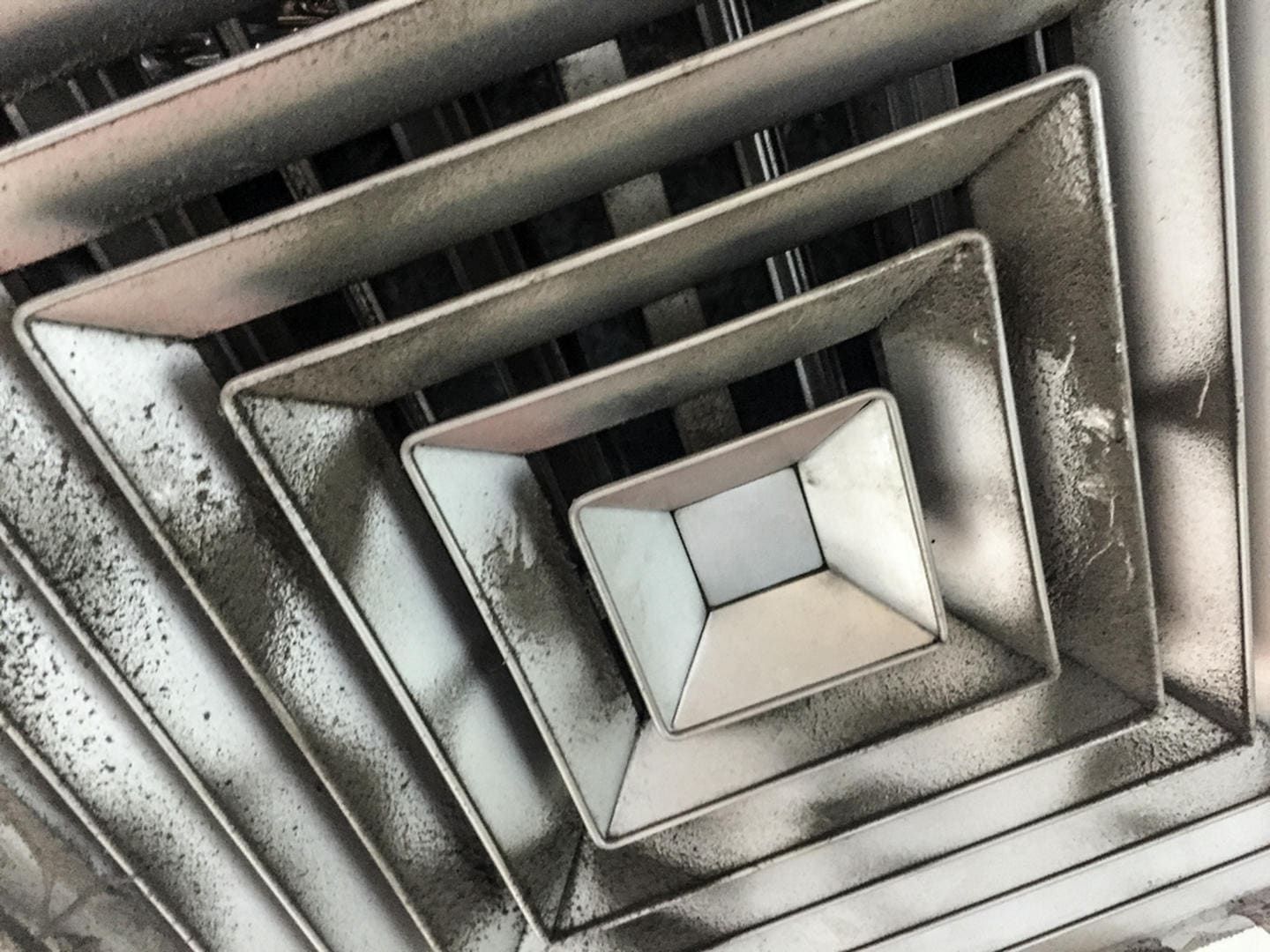 Close-up of a dirty, geometric air vent with square-in-square design.
