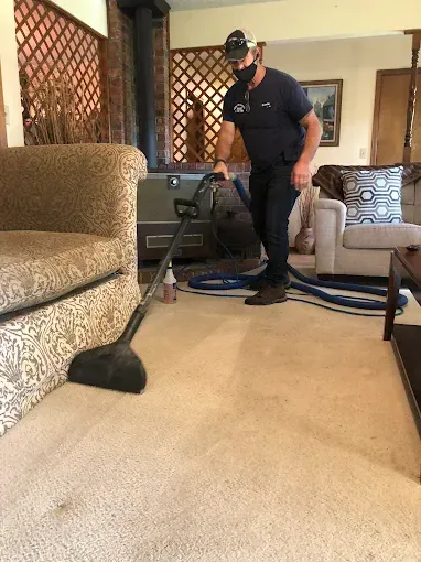 Man in mask cleaning carpet with a machine in a living room.