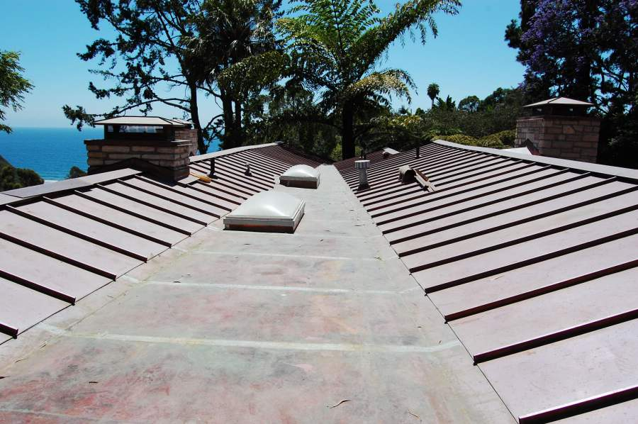 Brown metal roof with two chimneys, skylights, and a view of the ocean.