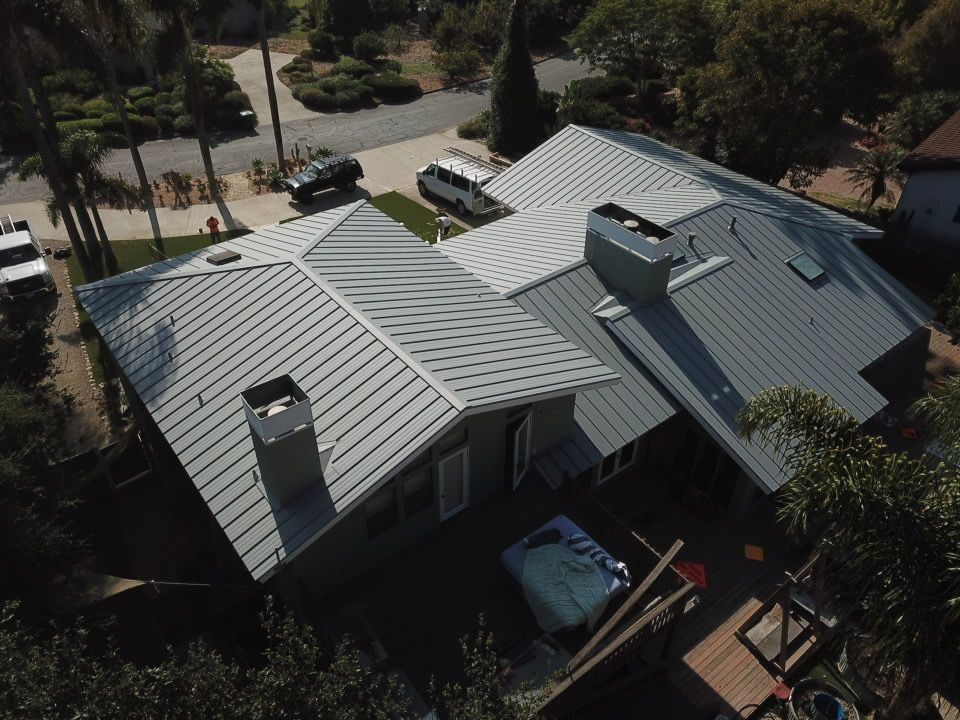 Aerial view of a house with a gray metal roof and surrounding trees and driveway.