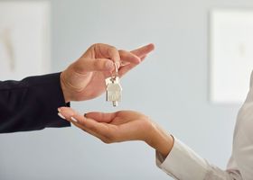A person hands over a house key to another person's open palm