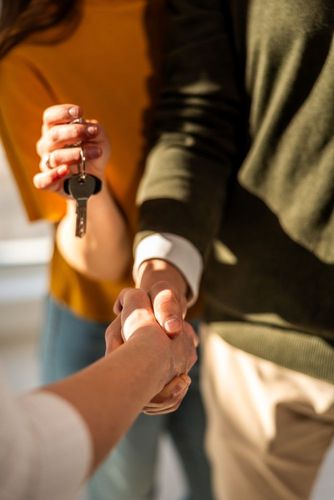 Person handing over keys while shaking hands in a warm indoor setting
