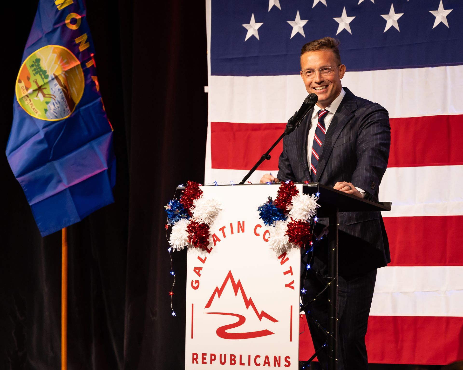 Man speaking at podium with California Republicans sign, in front of U.S. flag backdrop