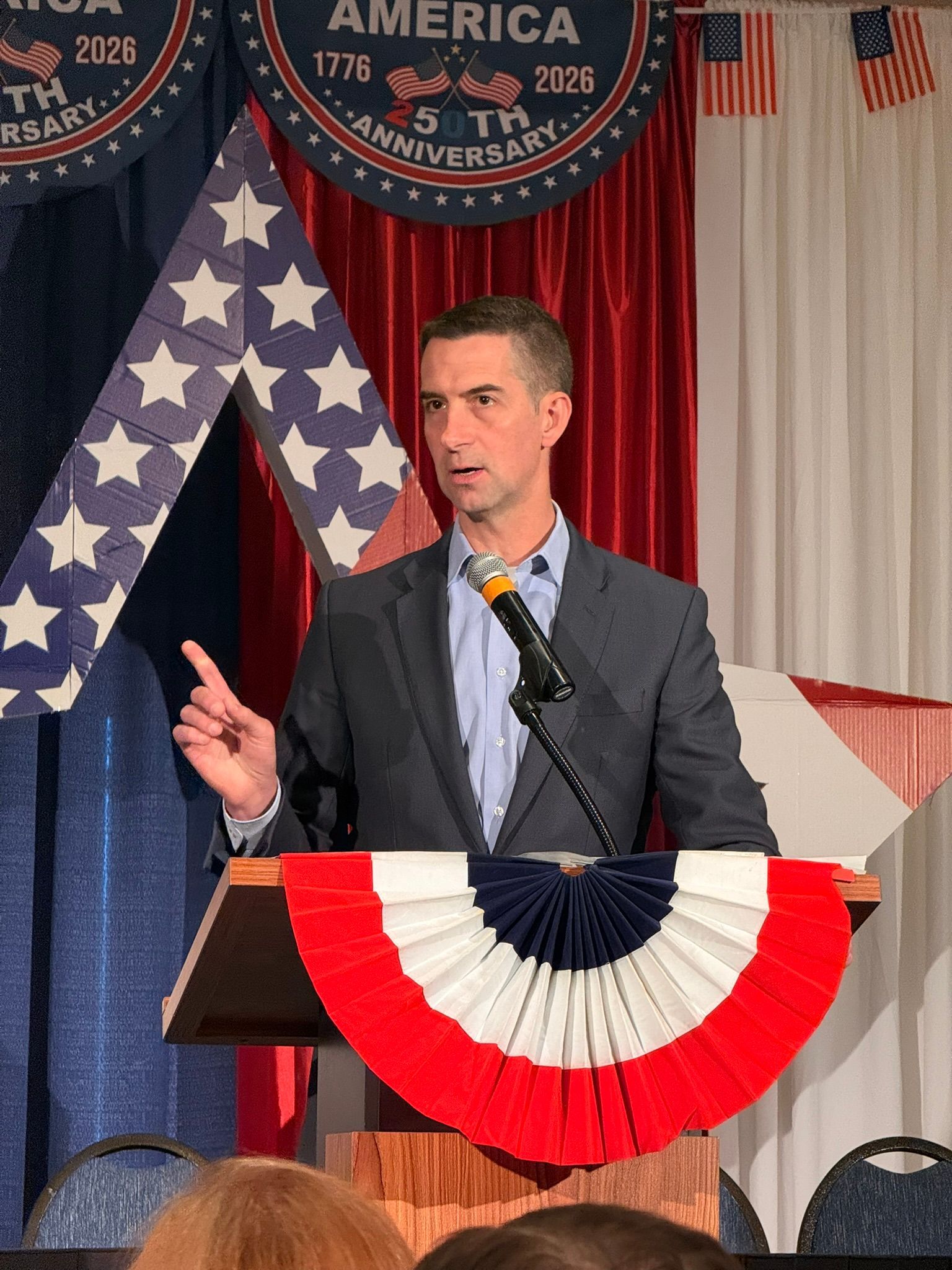 Man speaking at a podium with patriotic bunting and U.S. flags in the background