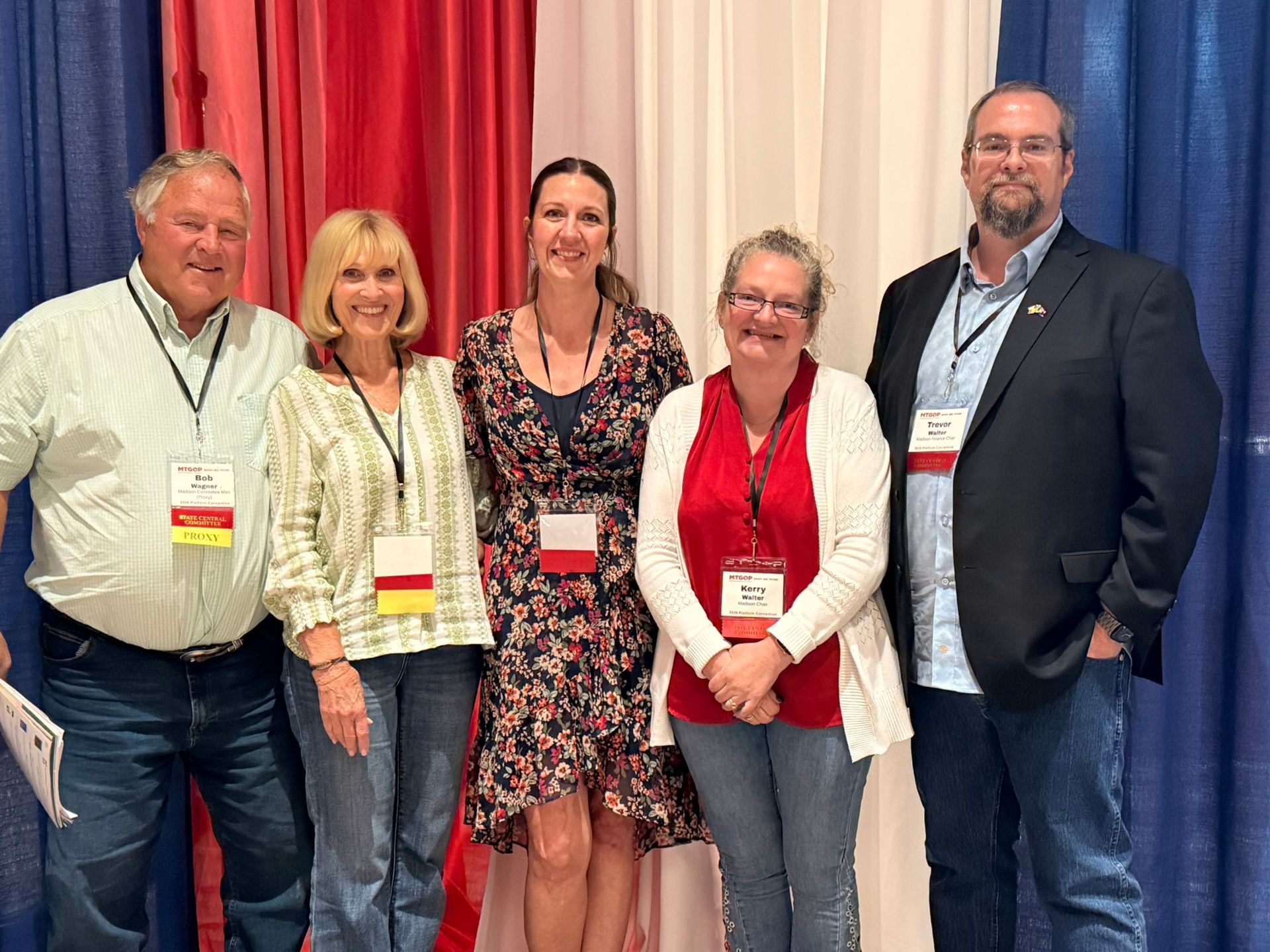 Five people posing in front of red and blue curtains at a conference.