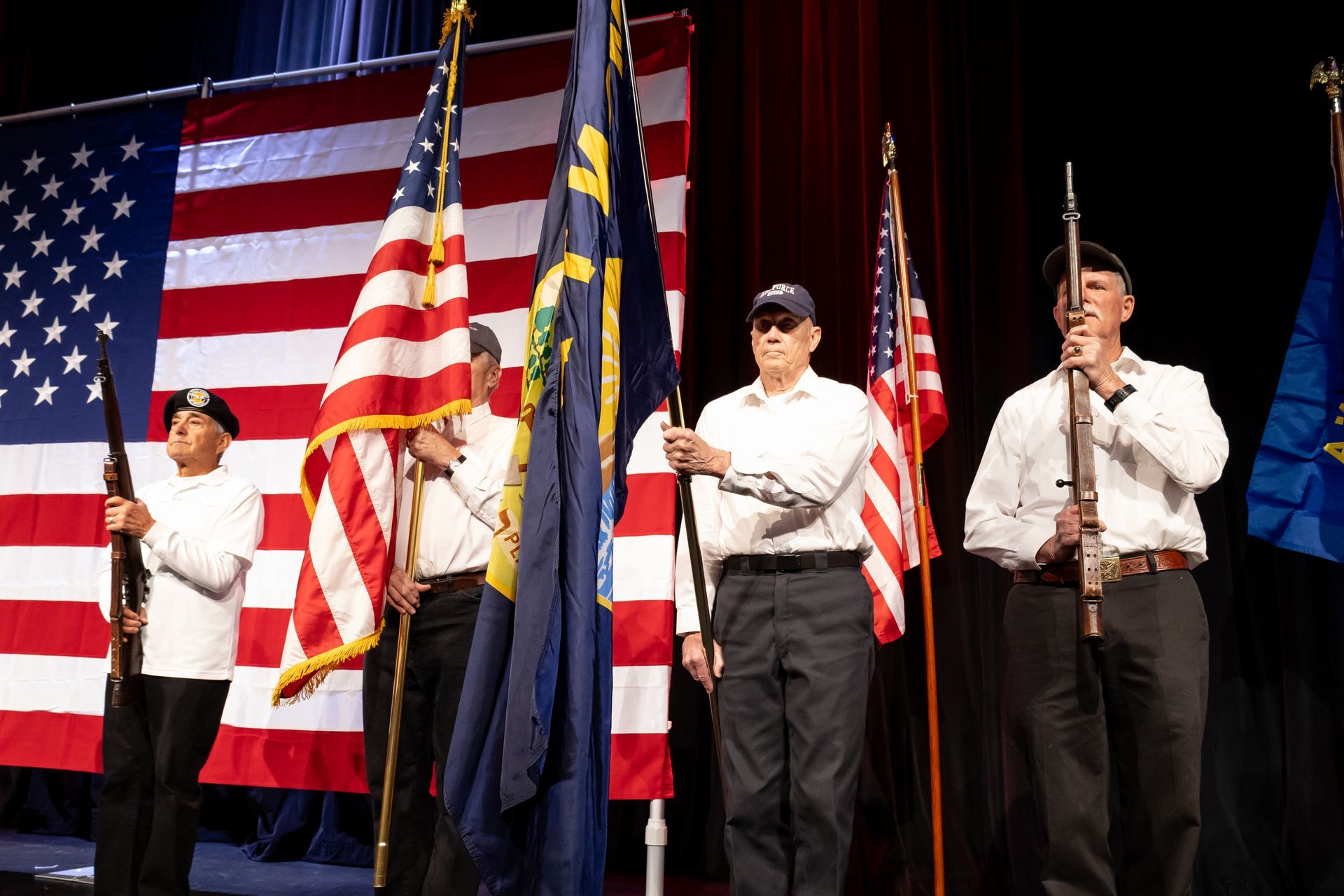Flag bearers standing on a stage with American flags and a large U.S. flag backdrop