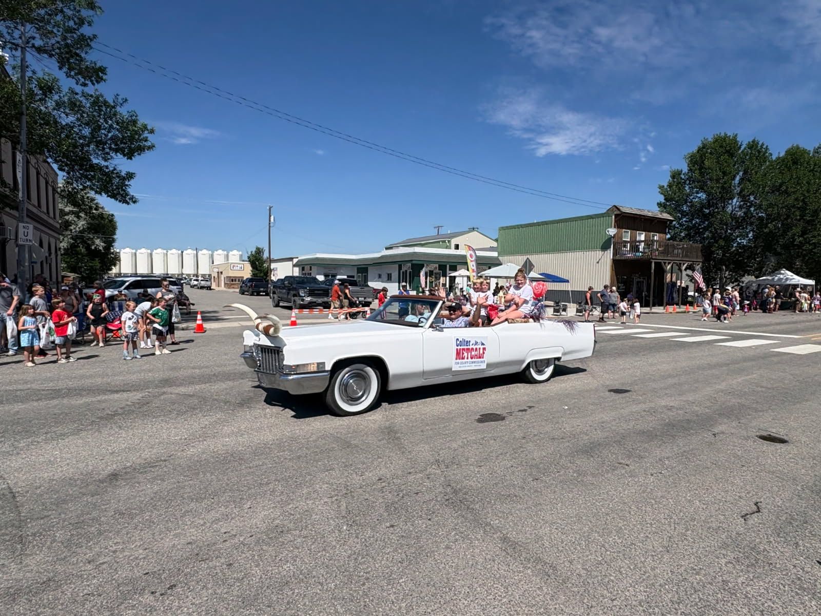 White vintage convertible in a parade on a sunny street with spectators lining the road.
