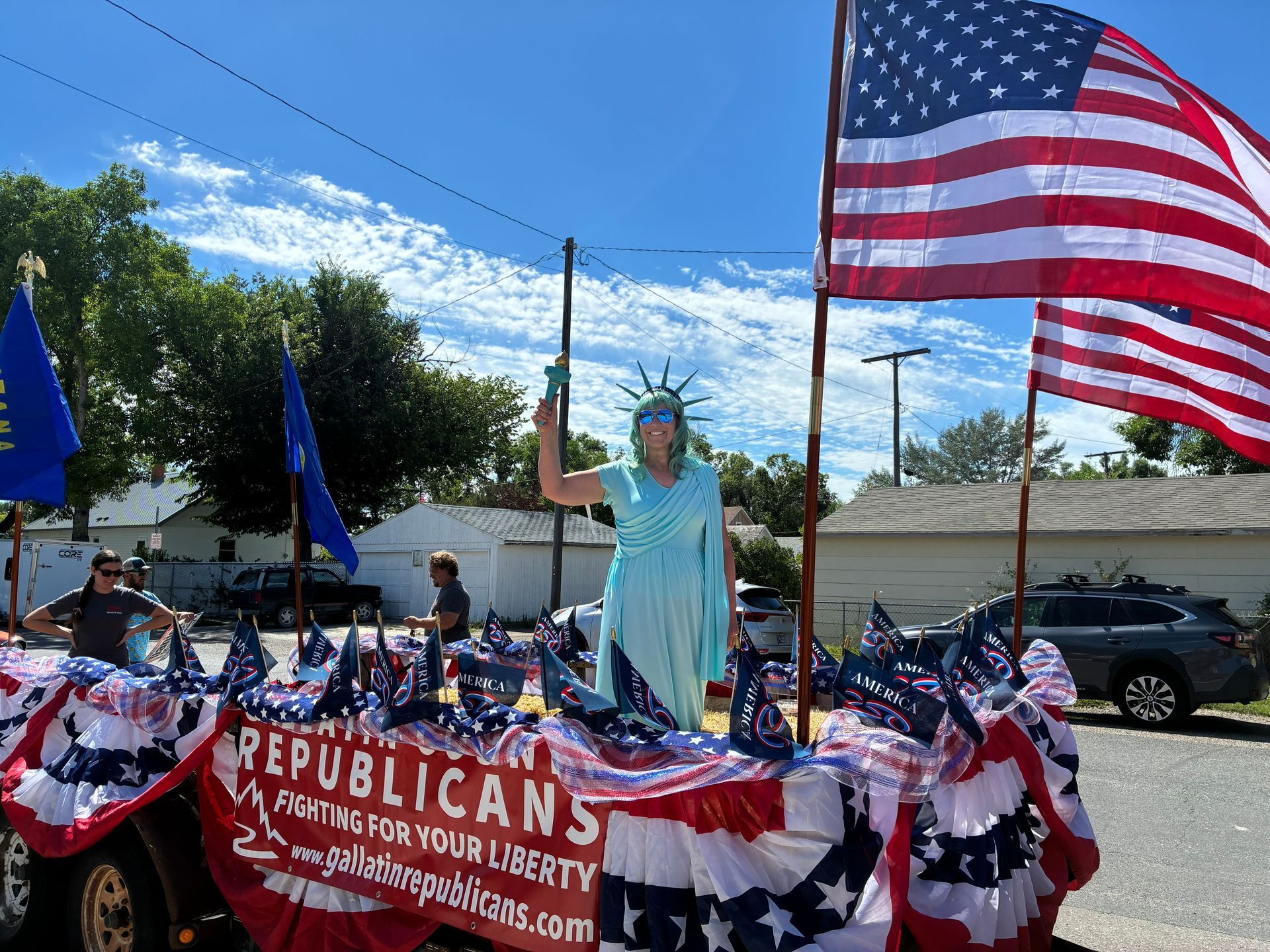 Pro-Trump parade float with U.S. flags, patriotic bunting, and Statue of Liberty figure on a sunny street