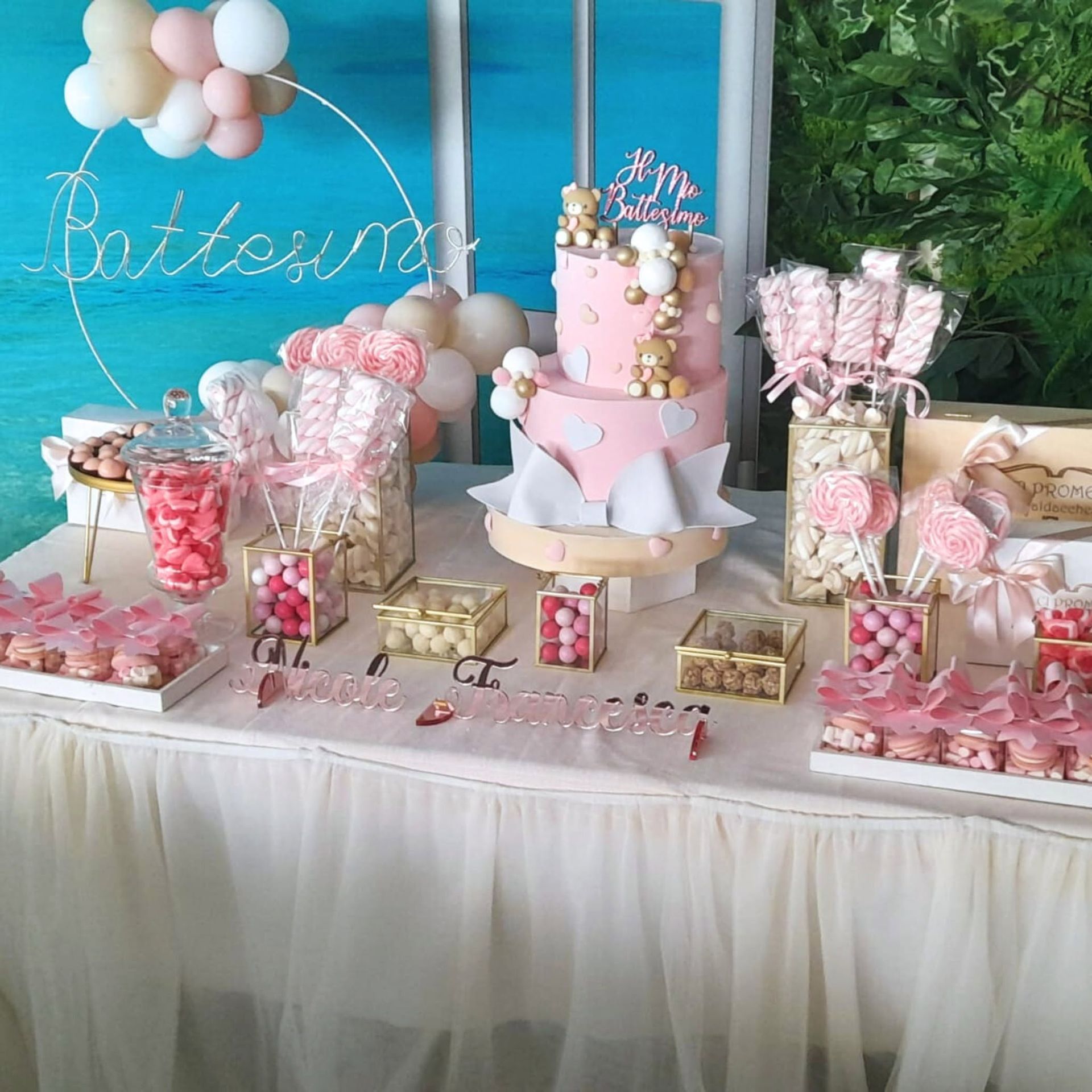 Tavolo dei dolci per una festa in rosa pastello con torta, palloncini e dolcetti su uno sfondo color verde acqua.