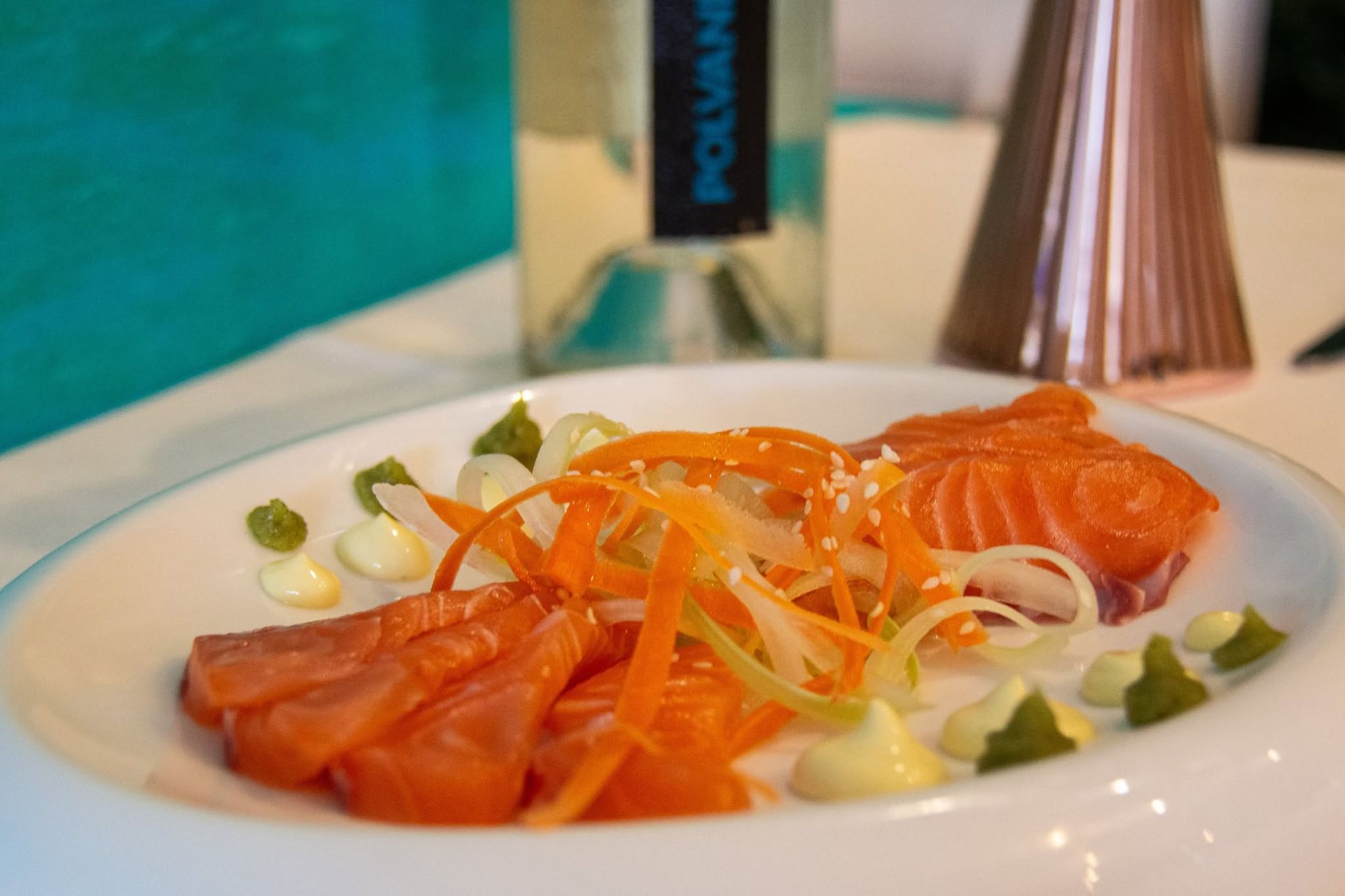 Sashimi di salmone servito con striscioline sottili di verdure e guarnizione su un piatto bianco.