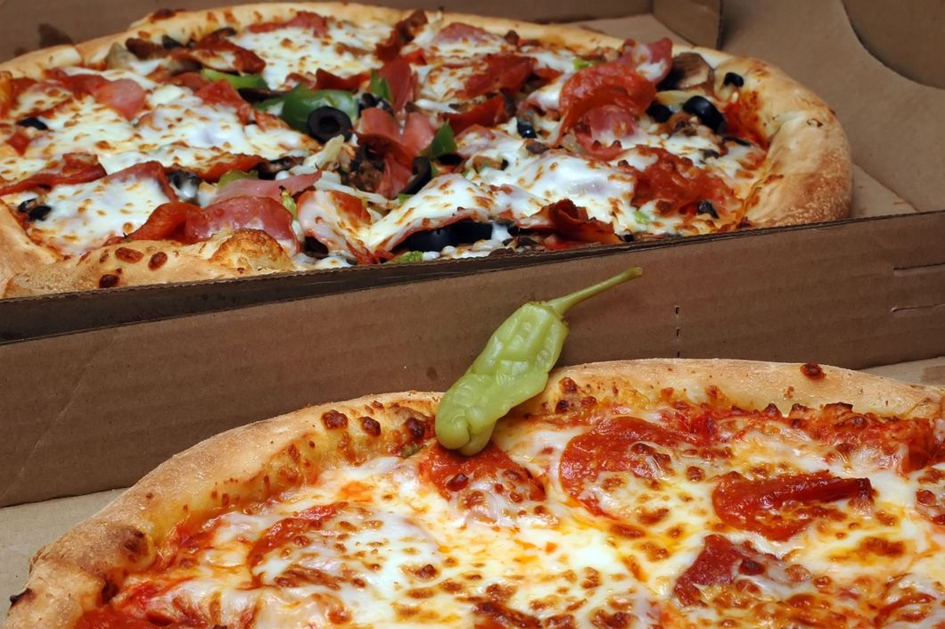 Due fette di pizza in una scatola, una con peperoni e verdure, una semplice con una foglia di basilico