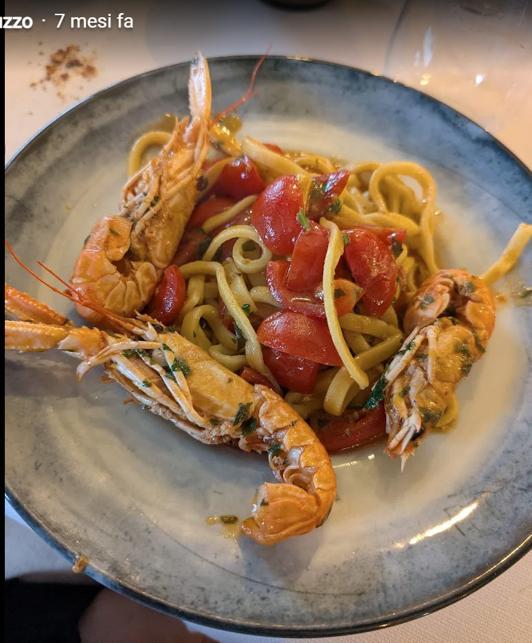 Piatto di pasta con gamberi e salsa di pomodoro in un piatto con bordo blu.