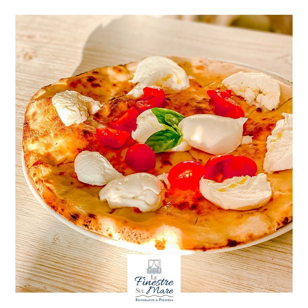 Pizza napoletana condita con mozzarella, pomodorini e basilico su un piatto bianco, in luce calda