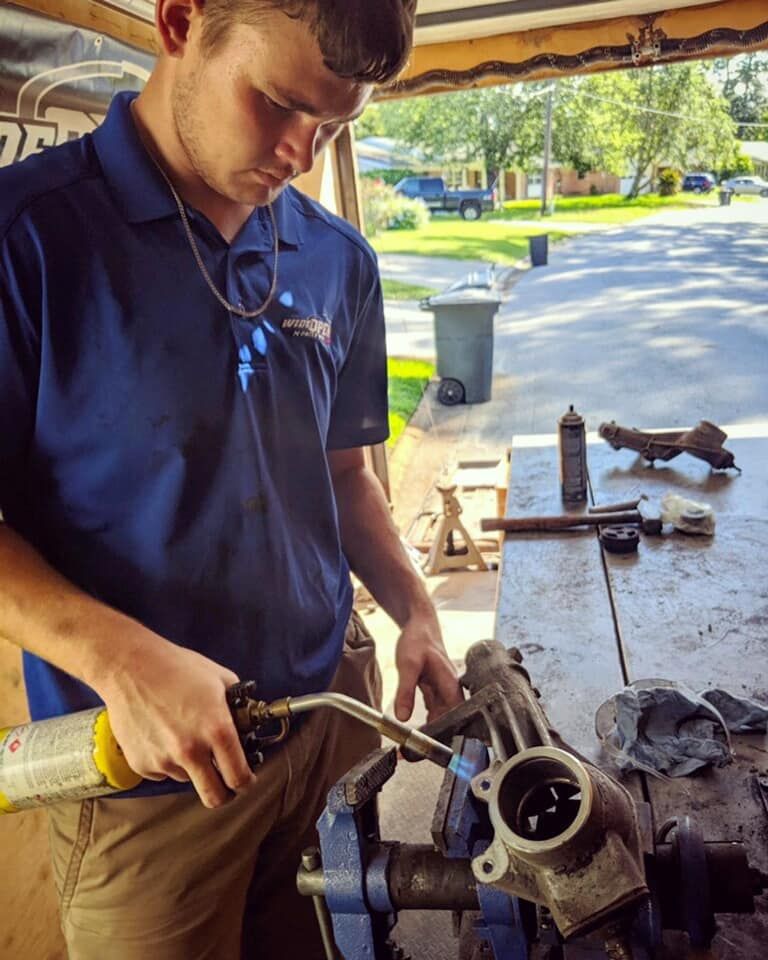 A man in a blue shirt is working on a piece of metal — St. Augustine, FL — Wide Open Mobile Tech