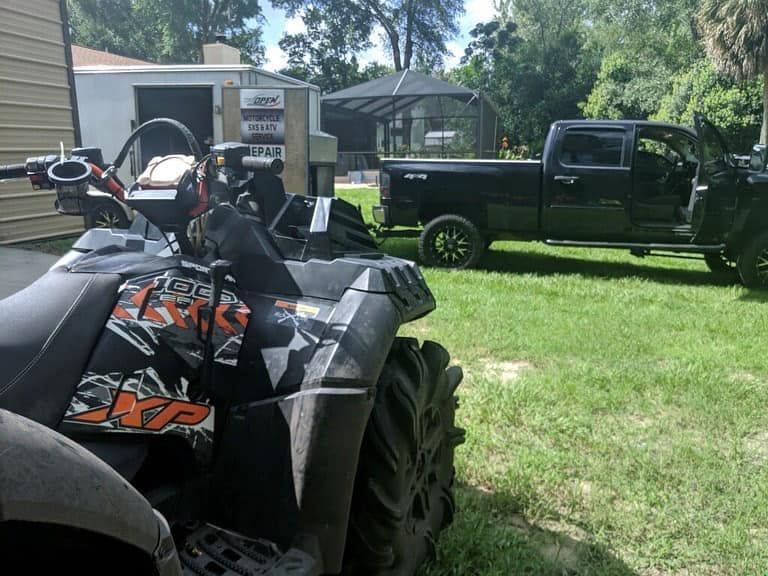 An ATV is parked next to a truck in a grassy yard — St. Augustine, FL — Wide Open Mobile Tech