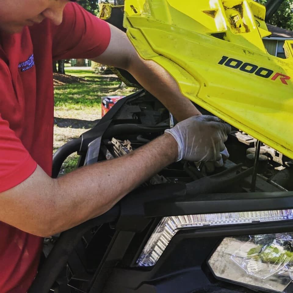 A man in a red shirt is working on a yellow snowmobile — St. Augustine, FL — Wide Open Mobile Tech