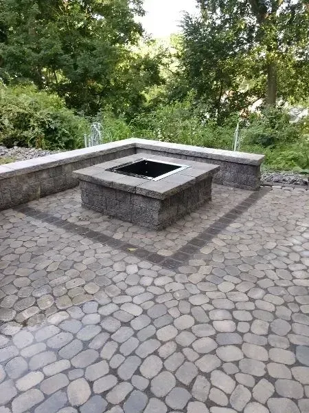 Stone patio with built-in fire pit, surrounded by low stone walls, set in a natural, tree-lined environment.