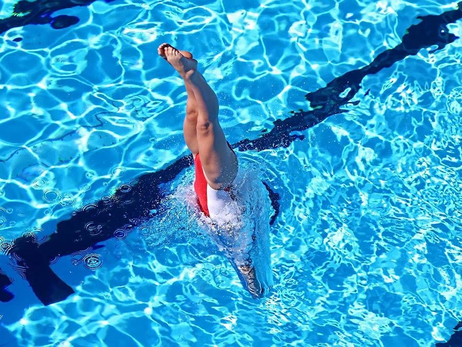 Swimmer doing a vertical dive in a bright blue pool lane