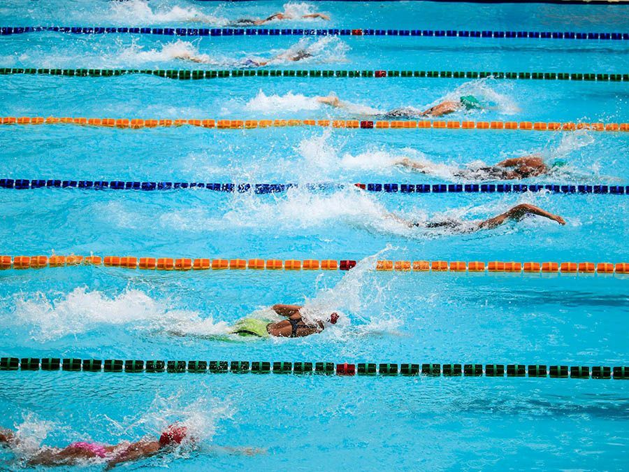 Competitive swimmers racing in lanes of a blue pool, splashing water during a freestyle race