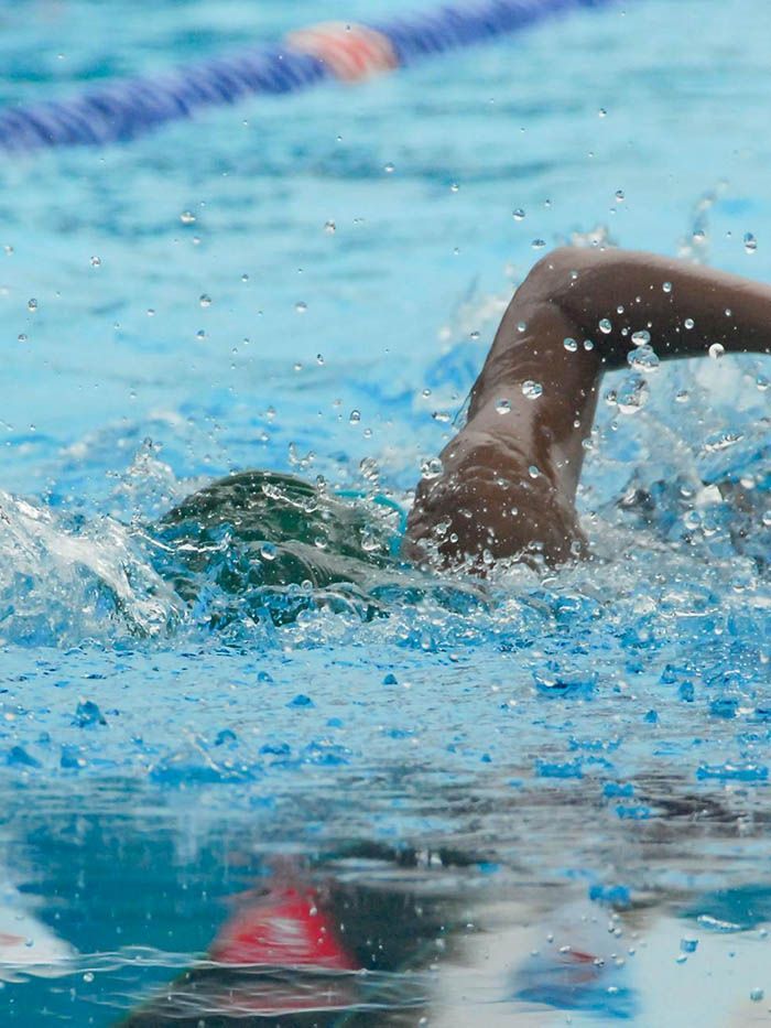Swimmer doing freestyle in a blue pool, arm raised amid splashing water.